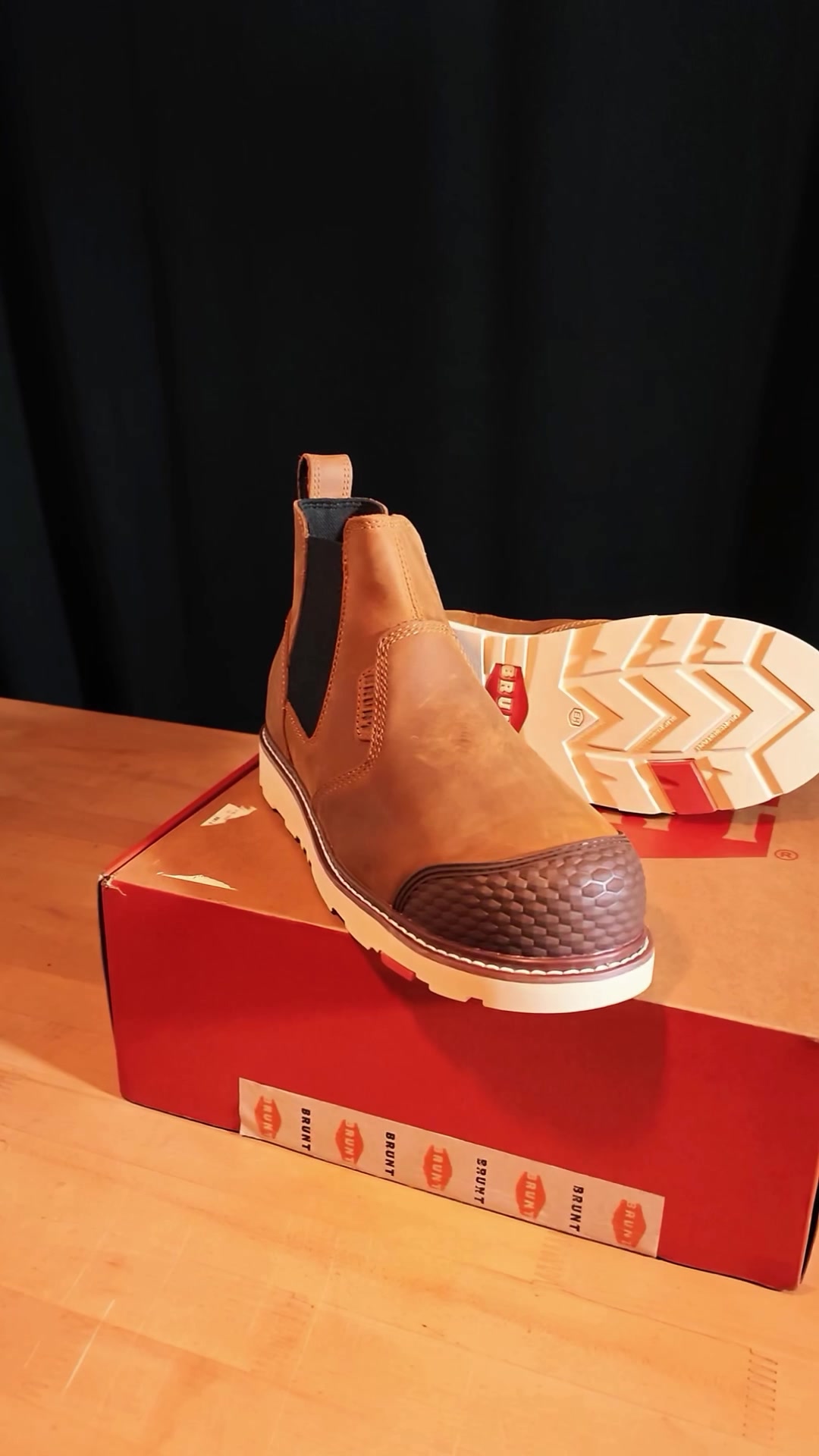 Tan leather work boot on a red shoebox against black drapes